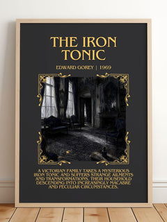 The Iron Tonic Minimalist Book Poster by Edward Gorey – framed print leaning on a wooden floor