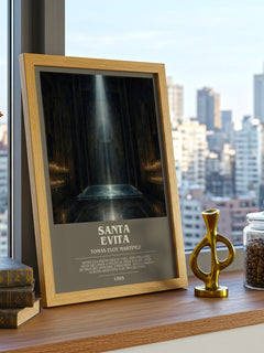 Santa Evita Bookish Wall Art by Tomás Eloy Martínez – framed print on a city-view windowsill